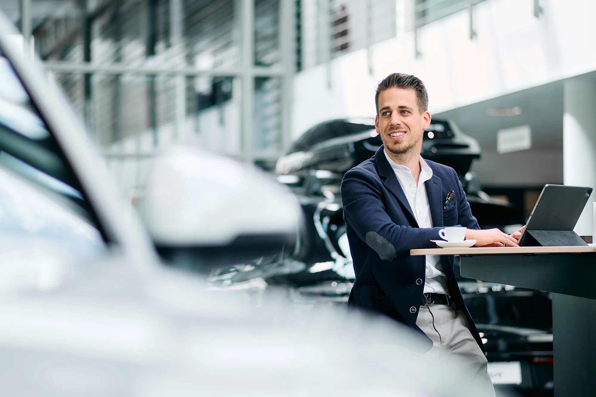 Businessfotos Düsseldorf 3 Ein Berater sitzt mit seinem Tablet in einem hellen Autohaus an einem Stehtisch