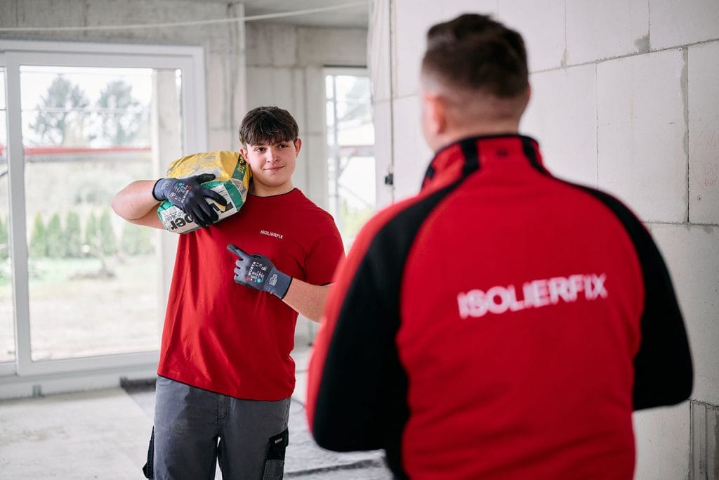 Handwerksfotografie - Authentische Bilder für ISOLIERFIX 5 Ein Handwerker trägt einen Zementssack auf der Schulter und blickt lachend zu seinem Kollegen