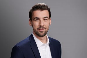 Professioneller Headshot eines jungen Geschäftsmannes in Hemd und Jacket vor grauem Hintergrund, Mitarbeiterfotos Köl