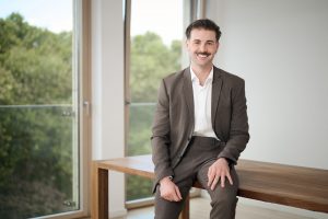 Mann im Anzug sitzt lässig auf einem Tisch am Fenster