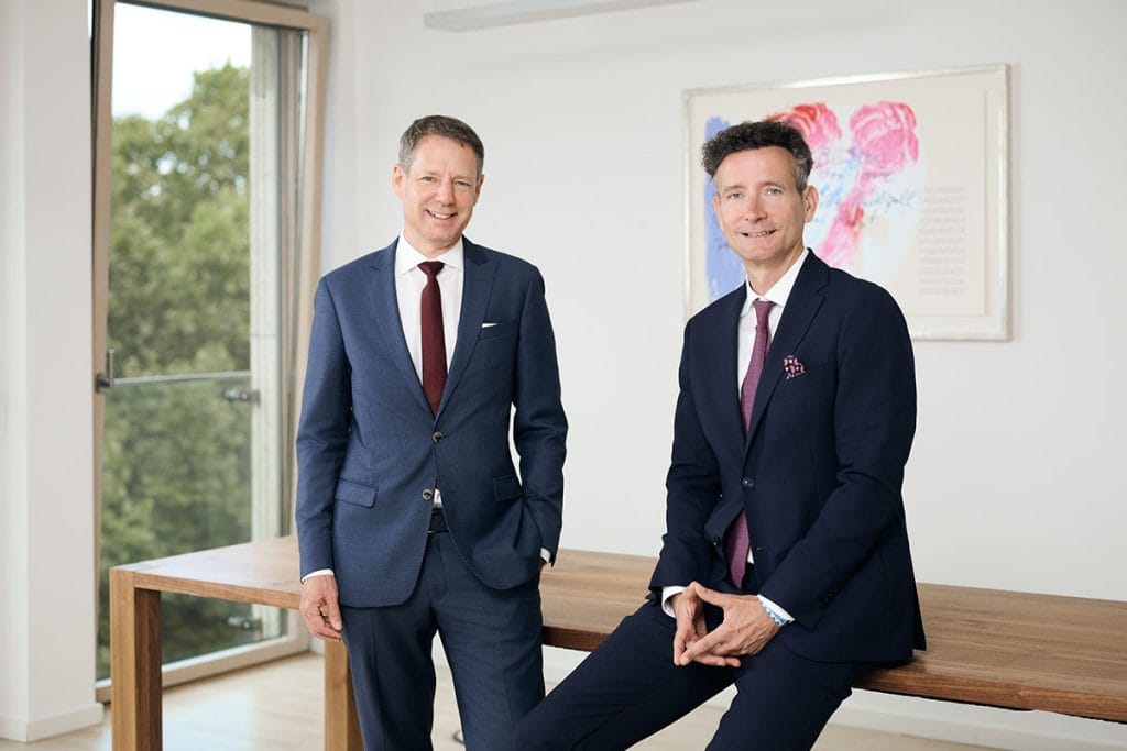 Businessfotos für Rechtsanwälte, Kanzleien und Steuerberater 4 Zwei Geschäftsmänner lehnen an einem Konferenztisch und lächeln in die Kamera